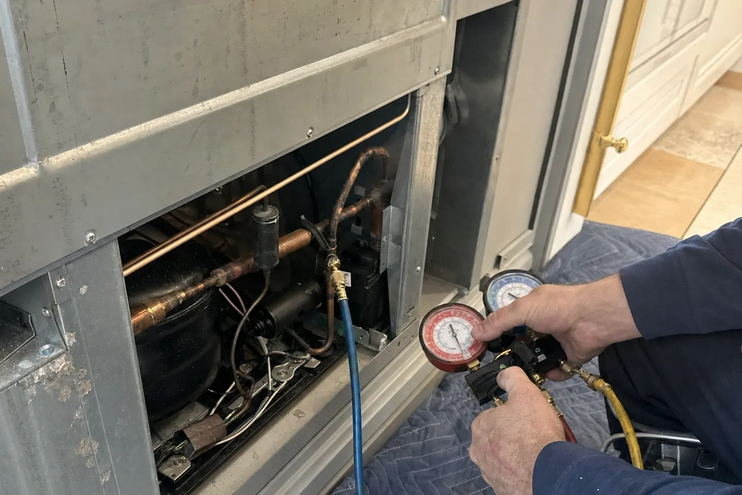Hands holding manifold gauges with both hoses run into the open machine compartment of a built-in